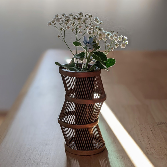 A hand-bent sepia Suruga bamboo single-flower vase with a unique undulating curve, intricate weaving at the base, and an accompanying dark wood stand. – view 2