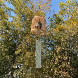 A delicately woven Suruga bamboo wind chime dome inspired by a Komuso monk's basket hat, containing a black Nambu iron bell.