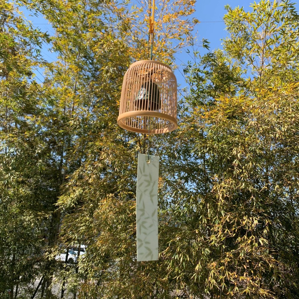 A delicately woven Suruga bamboo wind chime dome inspired by a Komuso monk's basket hat, containing a black Nambu iron bell.