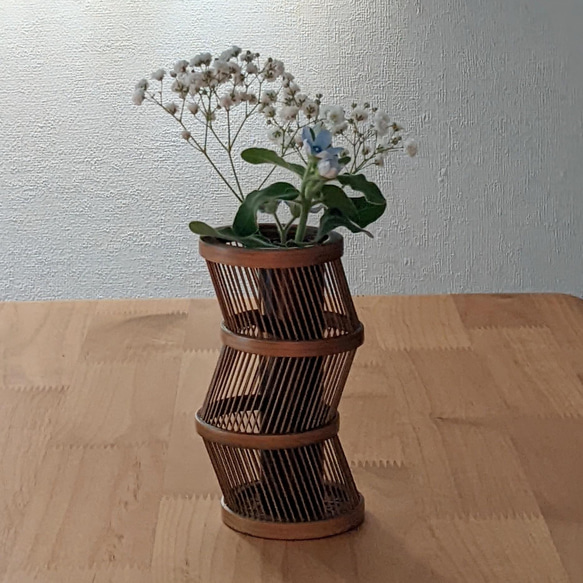 A hand-bent sepia Suruga bamboo single-flower vase with a unique undulating curve, intricate weaving at the base, and an accompanying dark wood stand. – view 9