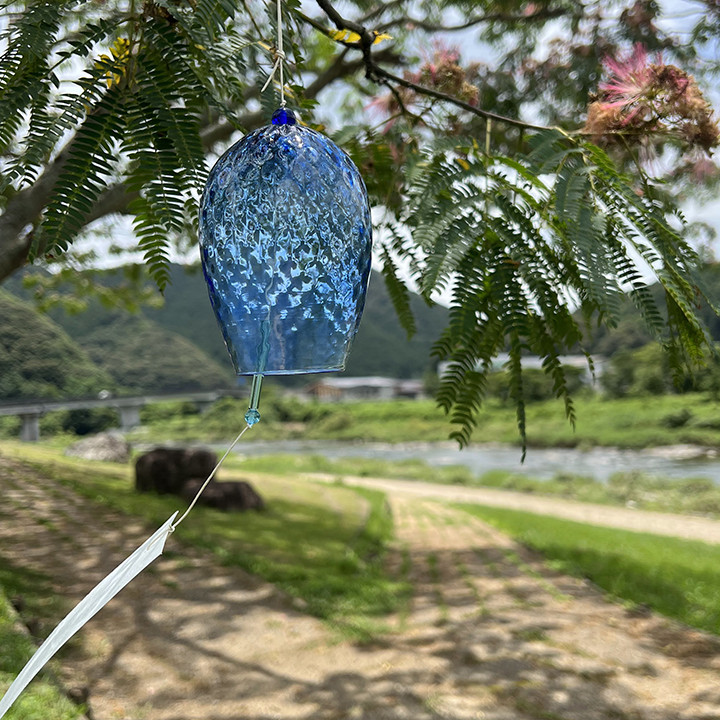 A handblown blue recycled glass furin wind chime with a white Ozu Washi paper wind catcher hanging from a wax cord.