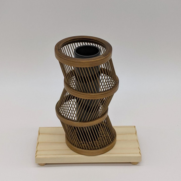 A hand-bent sepia Suruga bamboo single-flower vase with a unique undulating curve, intricate weaving at the base, and an accompanying dark wood stand. – view 4