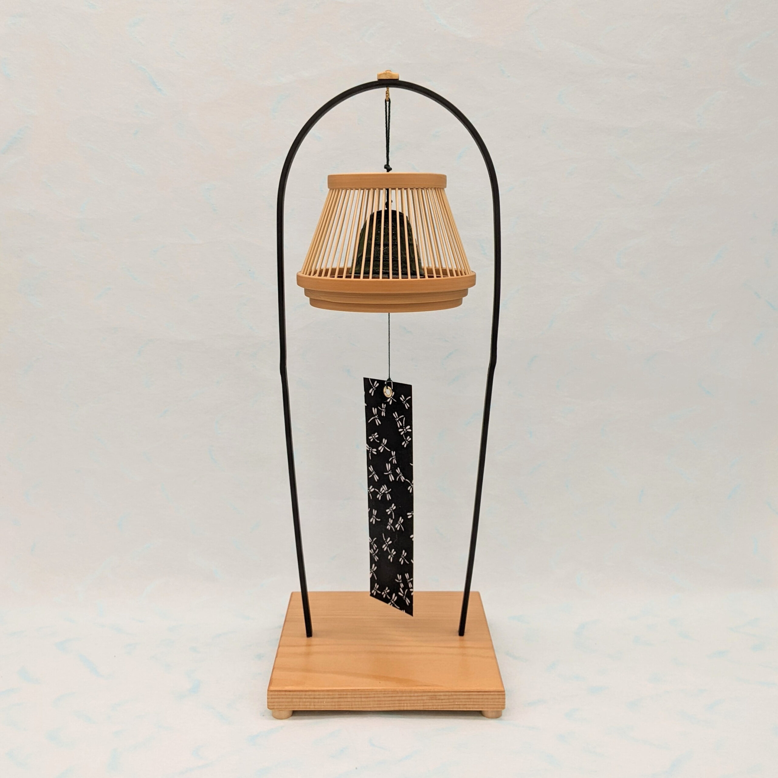 A conical Suruga bamboo lattice cage housing a dark Nambu iron wind bell, suspended from a tall tabletop wooden stand.