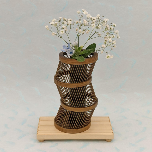 A hand-bent sepia Suruga bamboo single-flower vase with a unique undulating curve, intricate weaving at the base, and an accompanying dark wood stand. – view 3